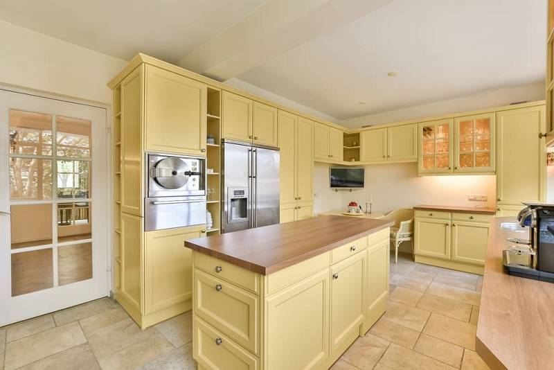 A,Kitchen,With,Yellow,Cabinets,And,Wood,Counter,Tops,In