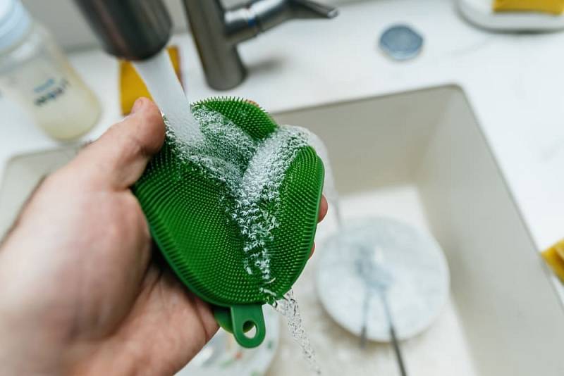 A,Hand,Using,A,Green,Silicone,Sponge,To,Clean,A